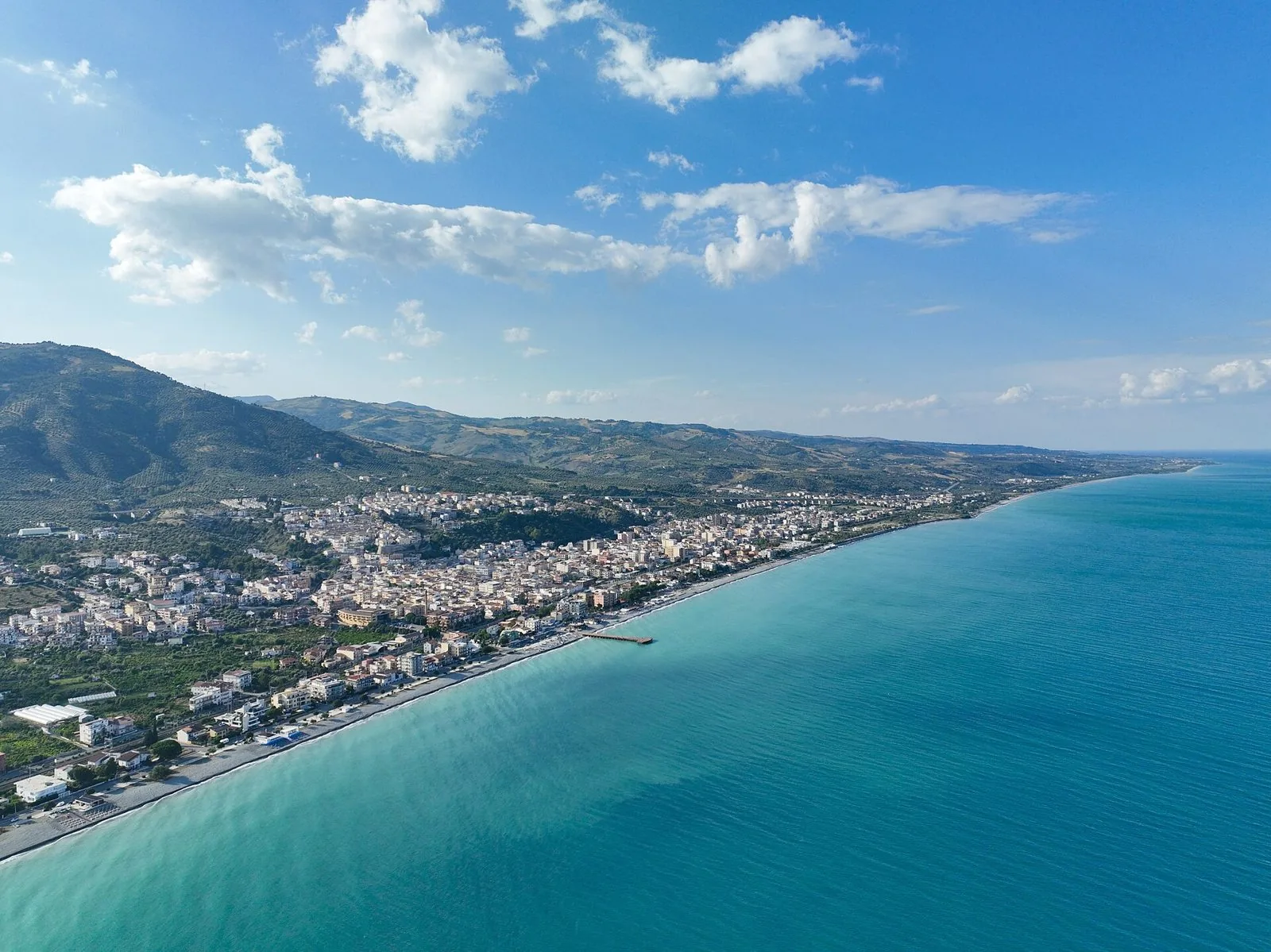 Veduta aerea di Trebisacce con il paese sulla collina, la marina lungo la spiaggia, il pontile e il mare turchese dello Ionio