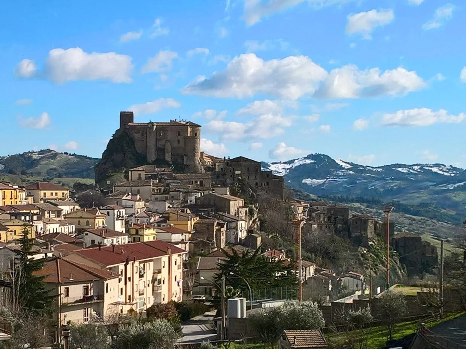 Panorama di Oriolo con il castello sulla rupe che domina le case del borgo e, sullo sfondo, colline con tracce di neve